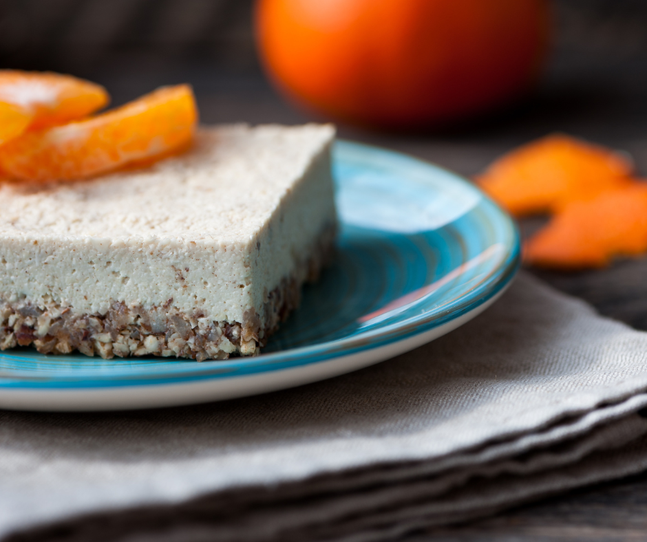 Cheesecake raw vegan cu pulbere de cătină, servit pe o farfurie albastră, decorat cu felii de mandarină – desert sănătos și delicios, fără coacere, cu strat crocant de migdale și curmale.