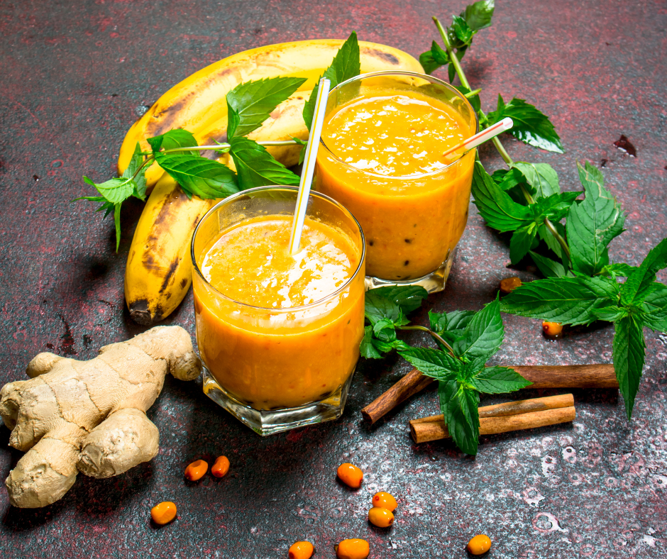 Smoothie de cătină și banane într-un pahar decorat cu mentă proaspătă, fructe de cătină și batoane de scorțișoară pe un fundal rustic roșu – băutură sănătoasă bogată în vitamine și antioxidanți.